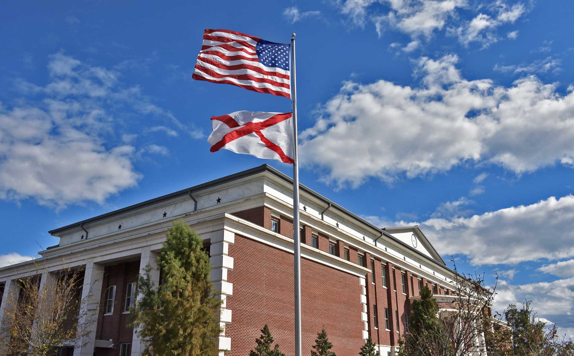 Courthouse flagpole with American and Alabama flags waving in the wind and blue partially cloudy skies