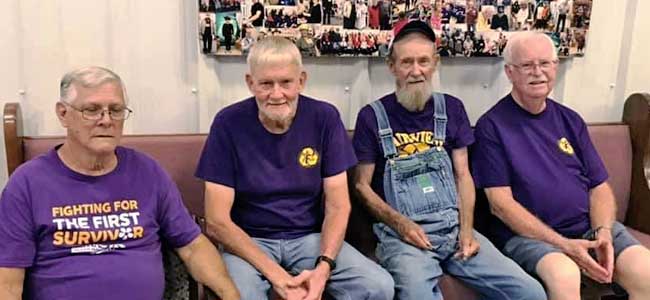 Four gentlemen from the Holly Pond Senior Center on bench with purple shirts