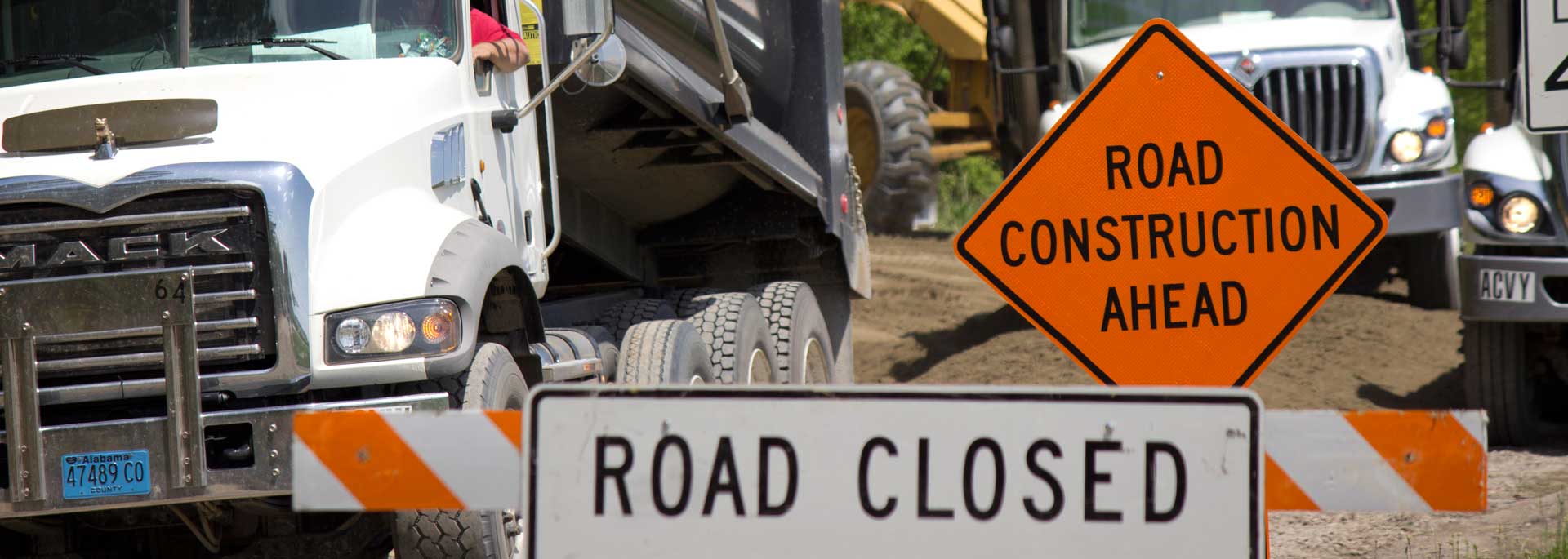 dump trucks on county road with signs reading Road Construction ahead, and  Road Closed.
